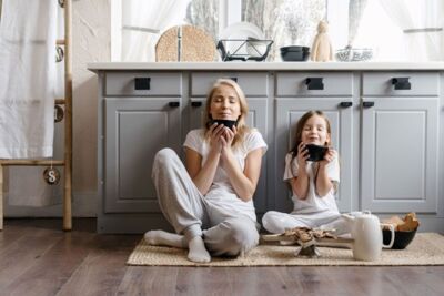 Mutter und Kind sitzen auf dem Küchenboden und halten eine Tasse Kaffee.